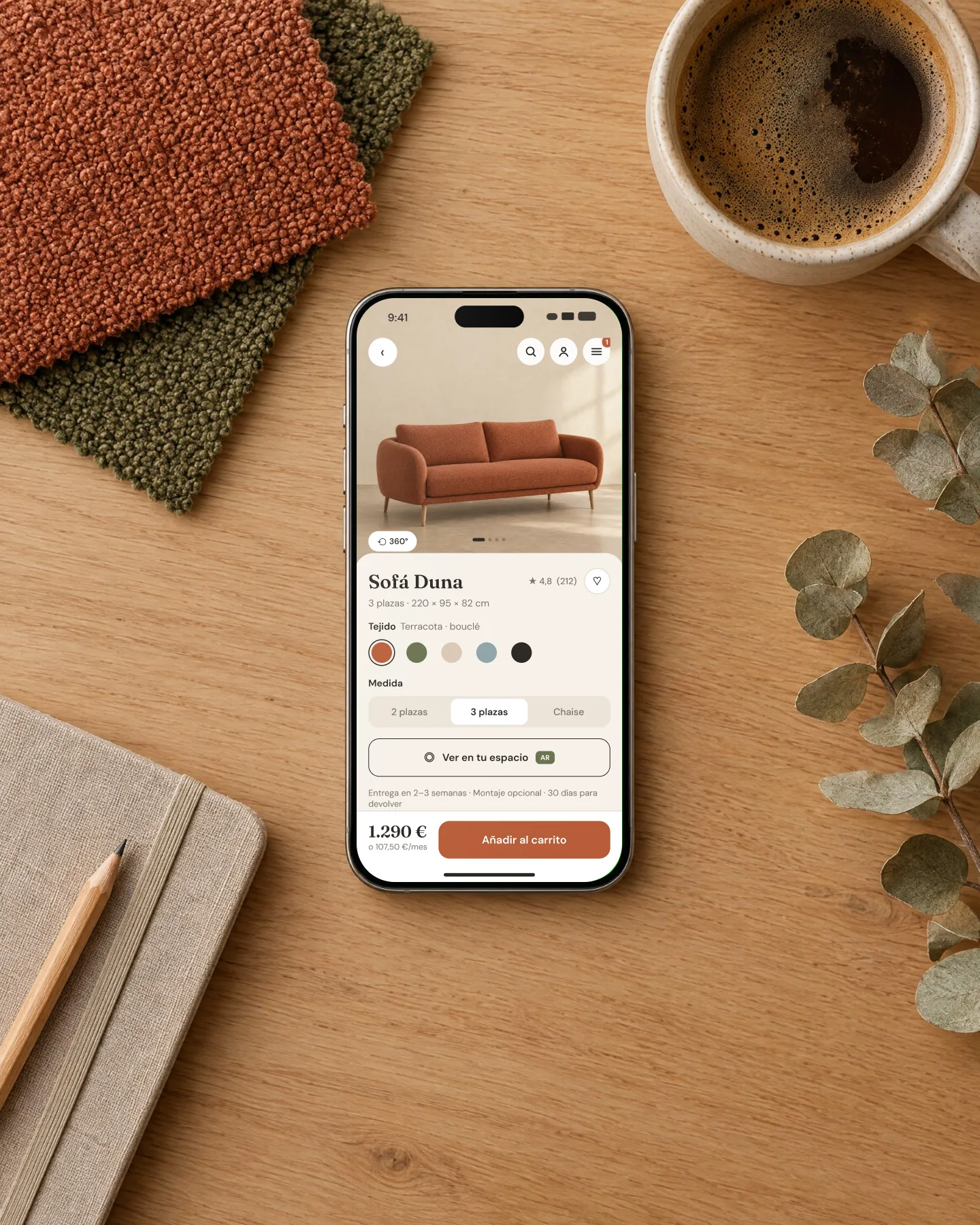 An iPhone on an oak desk showing the Duna sofa page, among fabric swatches, a coffee and a notebook